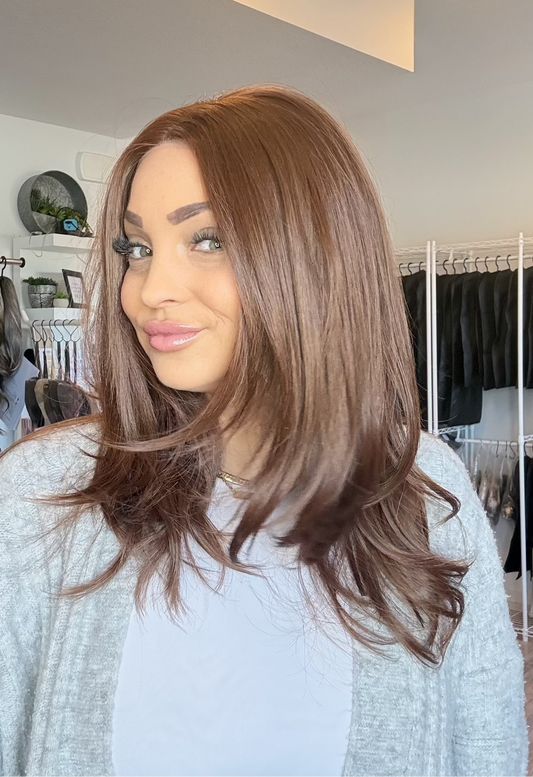 Woman with long brown hair in a room with clothing racks and a mirror.
