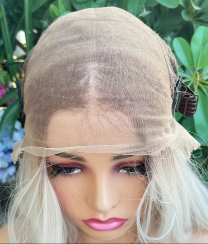 Person wearing a blonde wig outdoors with greenery in the background