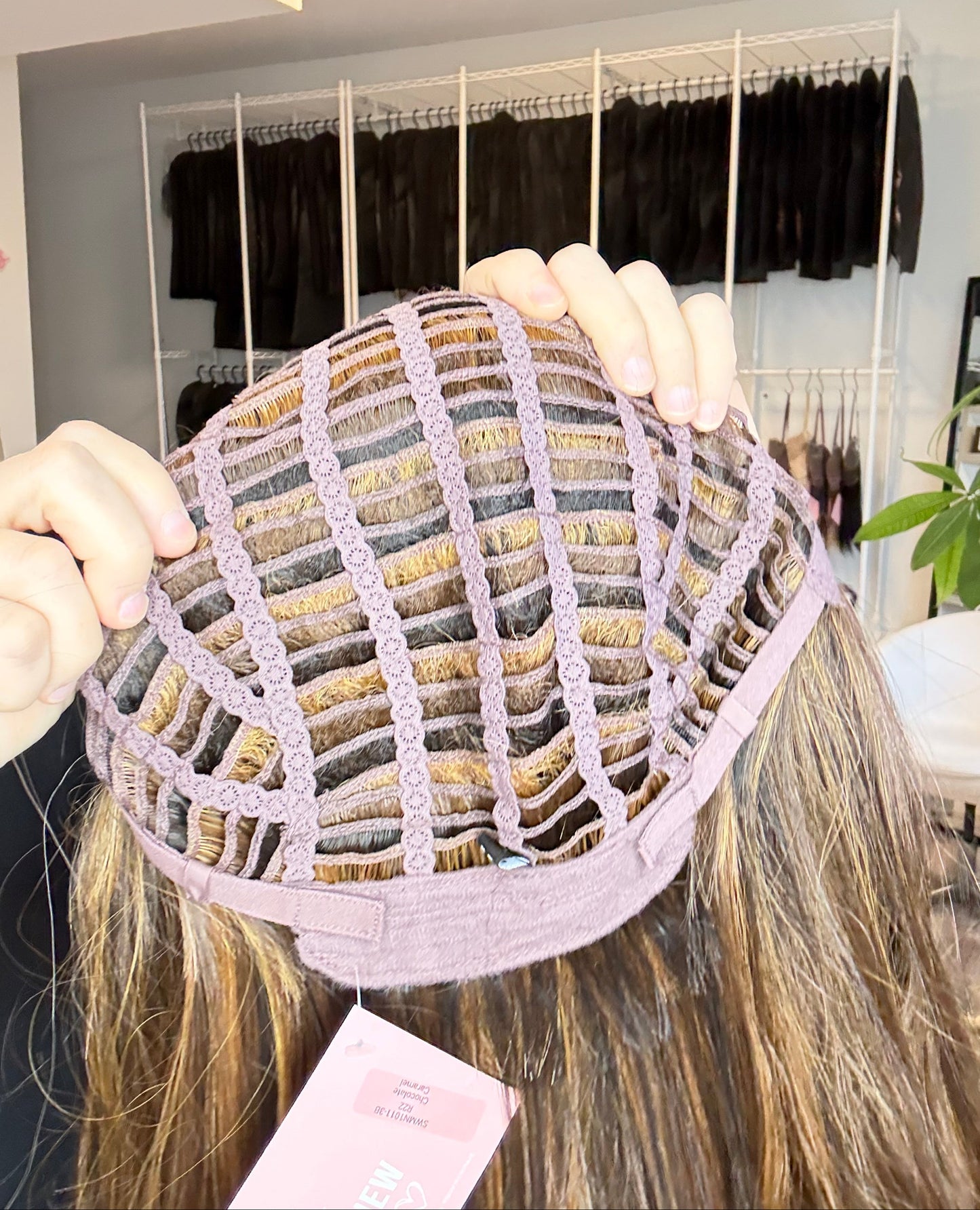 Person holding a wig with a display of hair extensions in the background