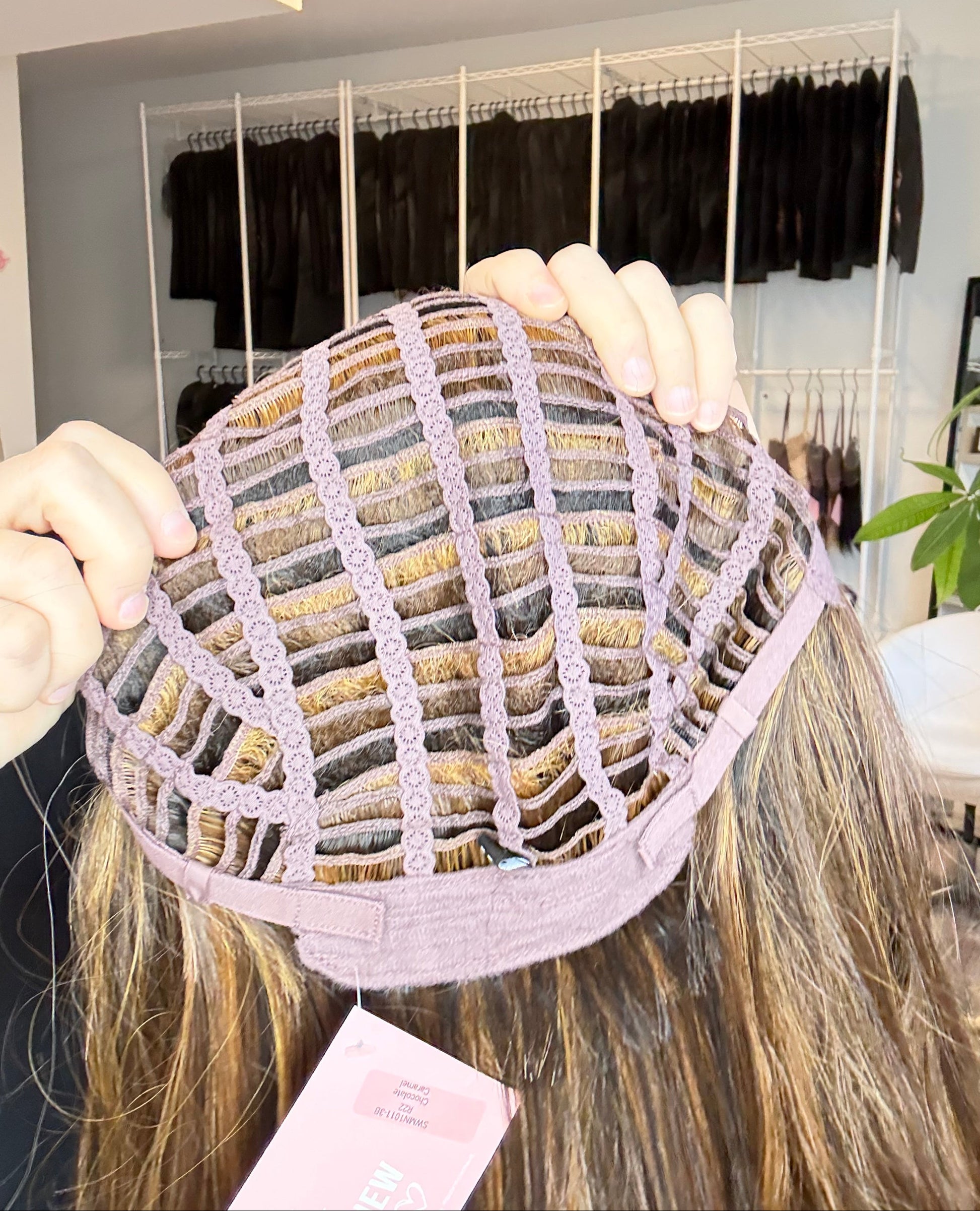 Person holding a wig with a display of hair extensions in the background