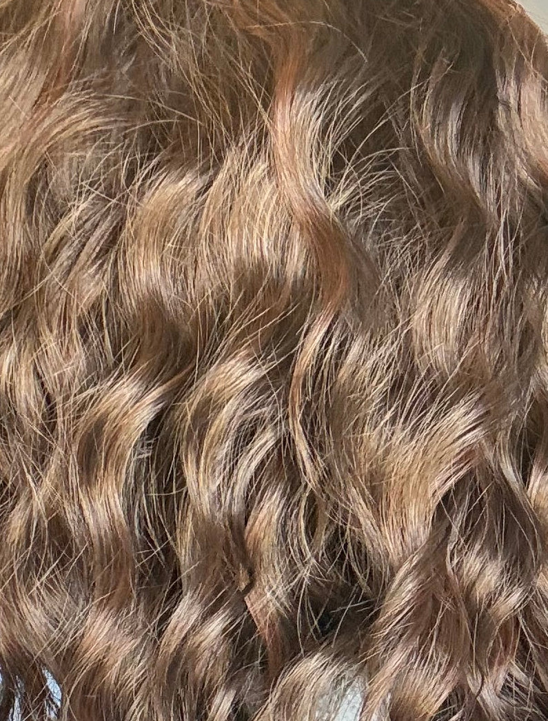 Close-up of a person with wavy hair in a room with a mirror and light fixture.