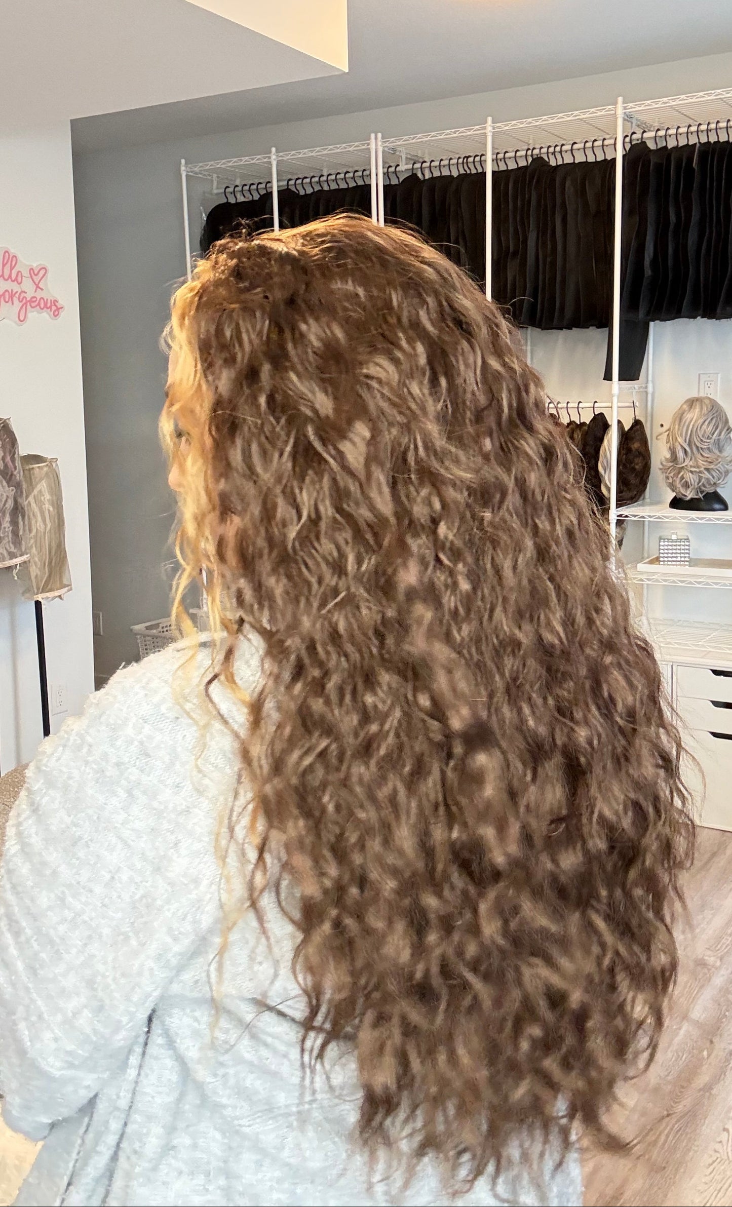 Person with long, wavy hair in a salon setting with mirrors and styling tools.