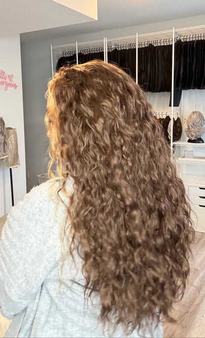 Person with long, wavy hair in a salon setting with mirrors and styling tools.