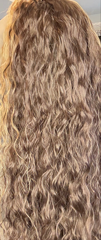 Person holding a long, wavy hair extension in a room with furniture and decor.