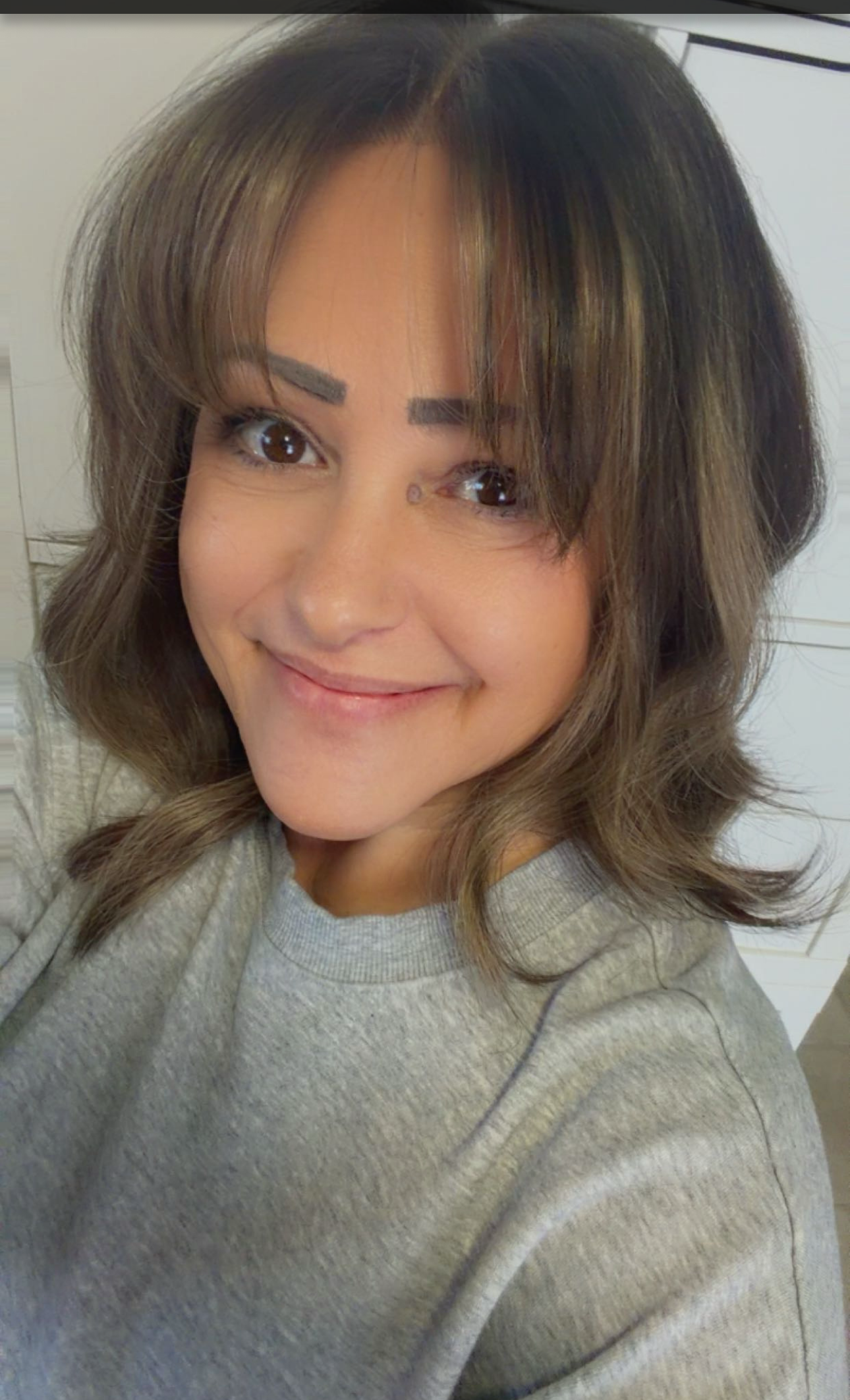 Person with shoulder-length hair wearing a gray sweater indoors