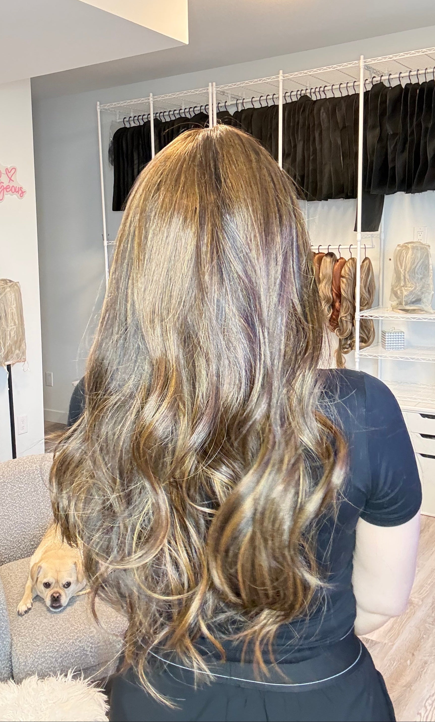 Person with long, wavy hair in a room with a mirror and light fixture.