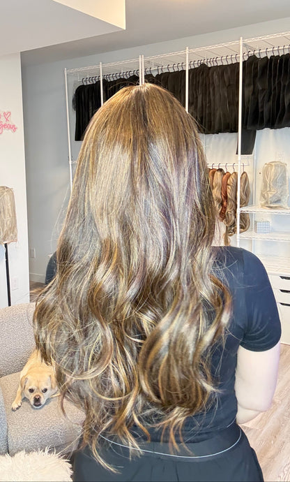 Person with long, wavy hair in a room with a mirror and light fixture.