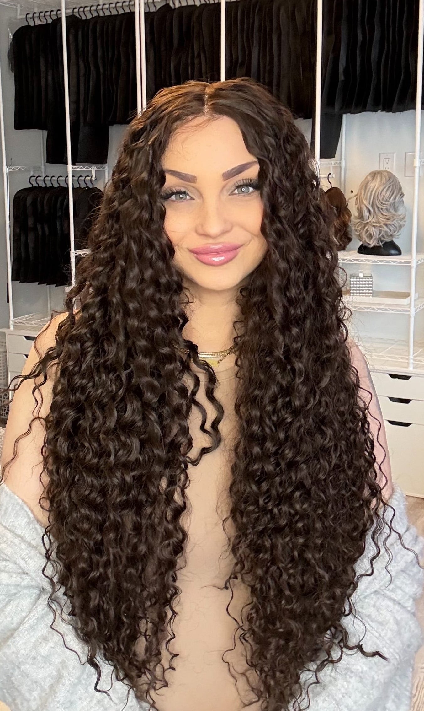 Woman with long, curly hair in a room with hair extensions displayed on racks.