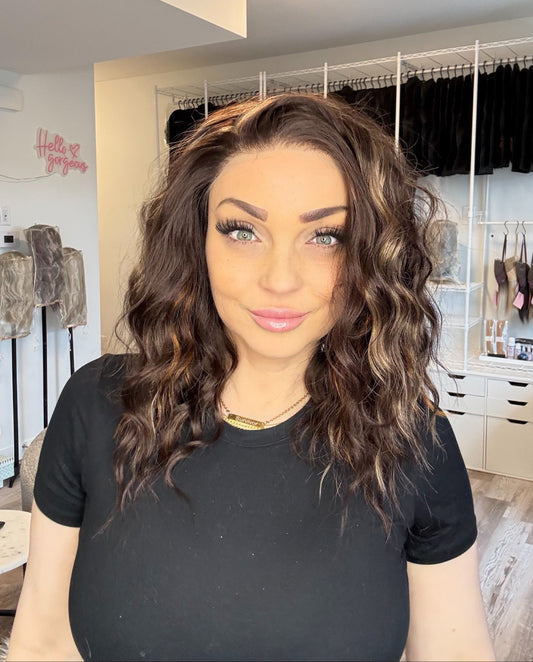 Woman with styled hair in a room with clothing racks and a mirror.