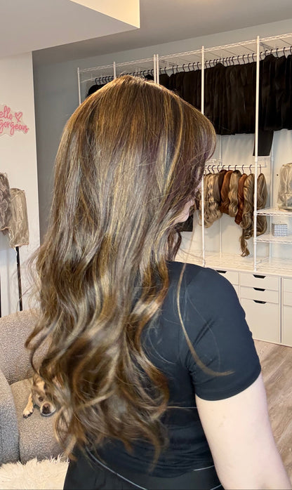 Person with long, wavy hair in a room with shelves and a mirror.