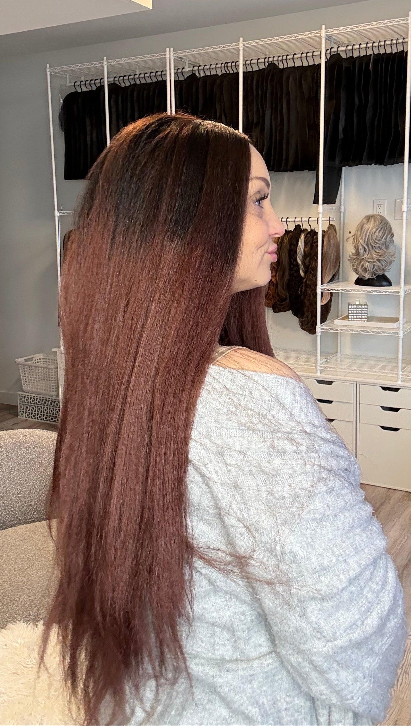 Woman with long hair in a salon setting, looking at herself in the mirror.
