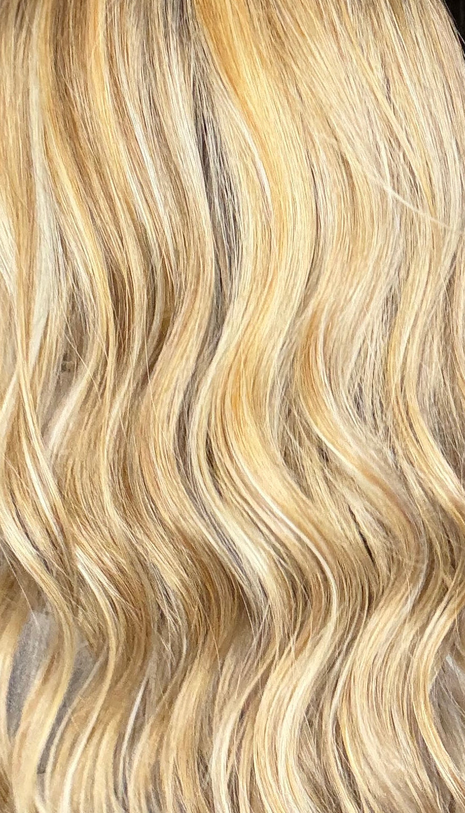 Blonde hair extensions held up in front of a mirror with hair color samples in the background.