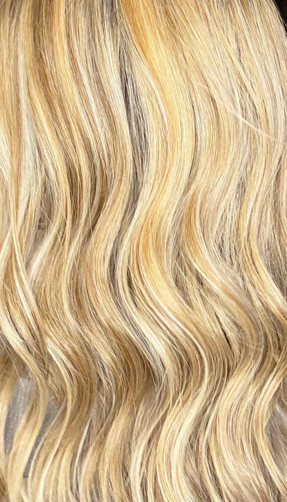Blonde hair extensions held up in front of a mirror with hair color samples in the background.