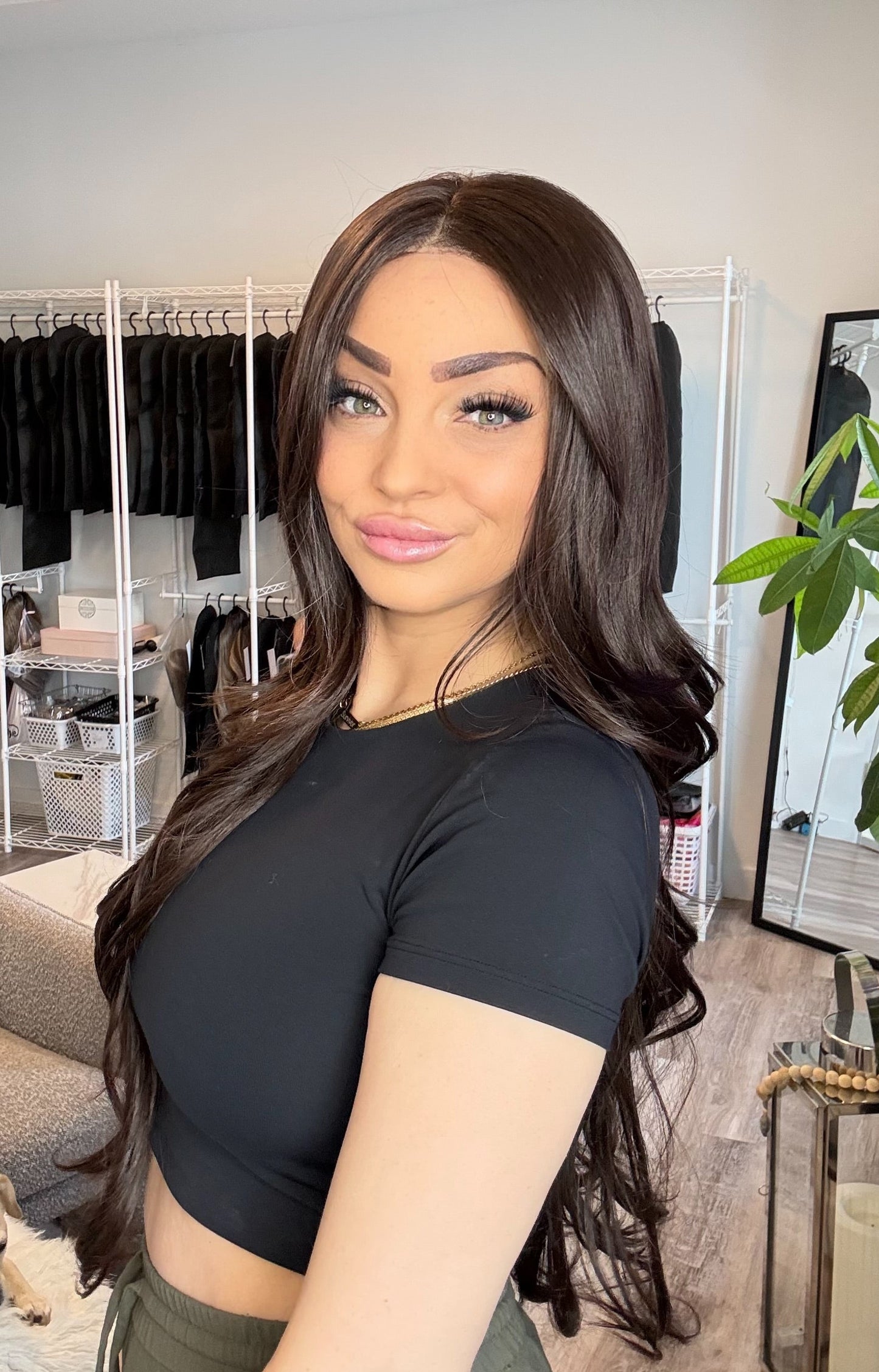 Woman taking a selfie in a room with a dog and clothing rack in the background