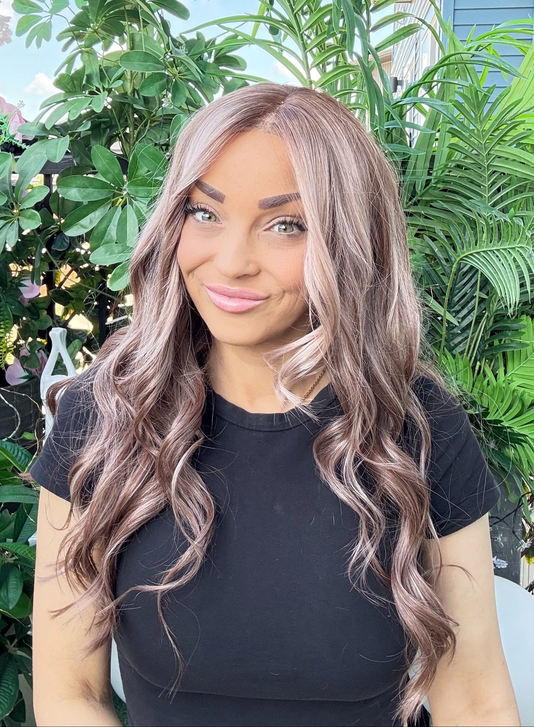 Woman with long, wavy hair standing in front of green plants