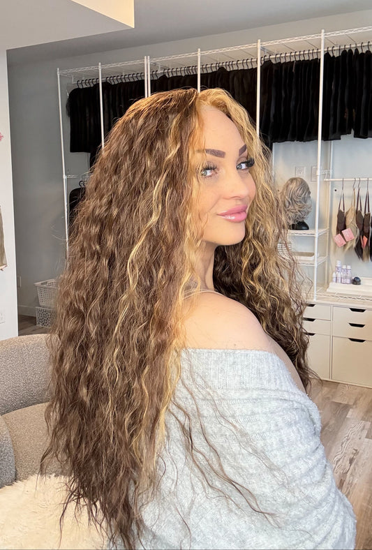 Woman with long, wavy hair in a room with mirrors and clothing racks.