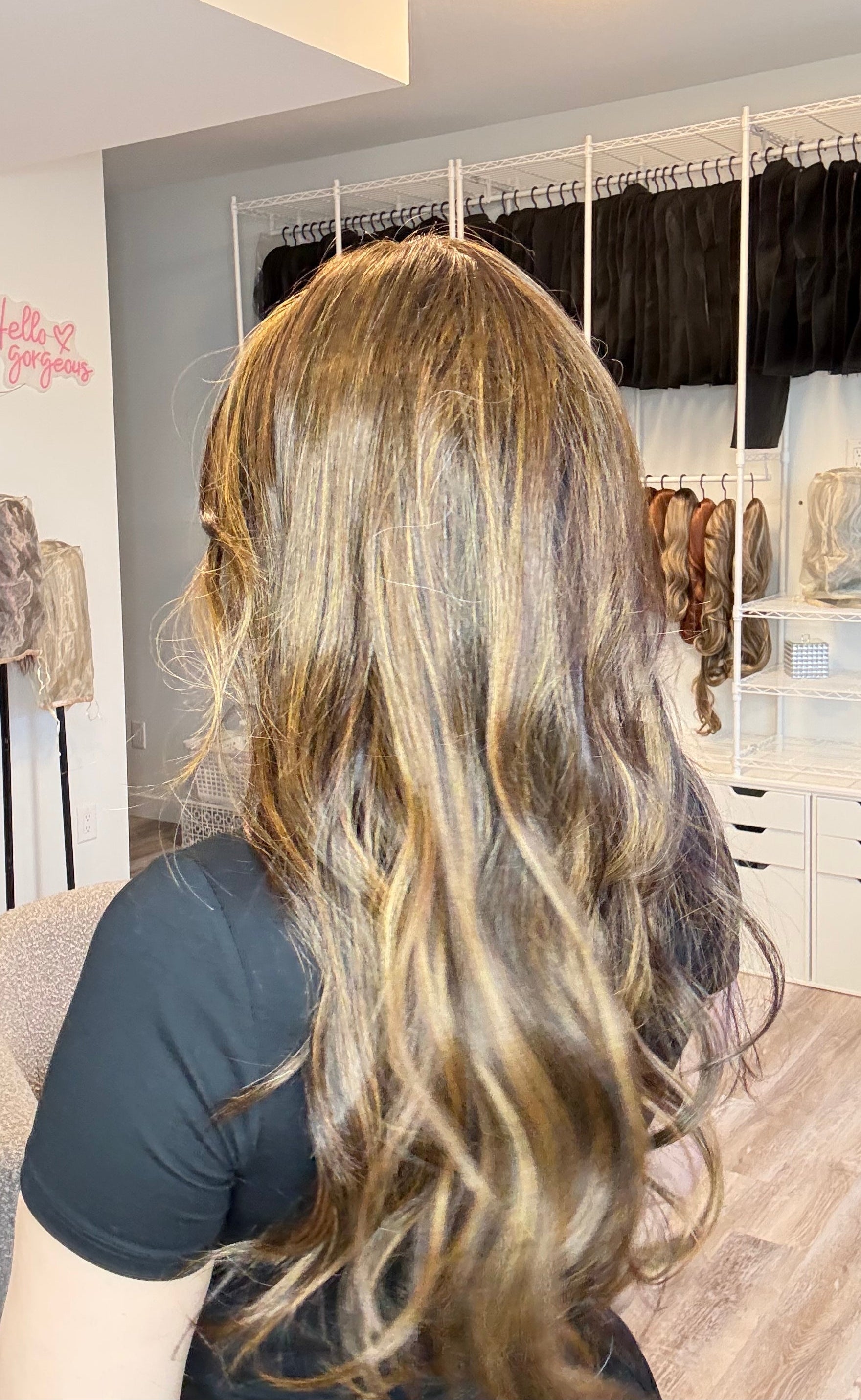 Person with long, wavy hair sitting in a salon chair with a mirror reflecting the room.