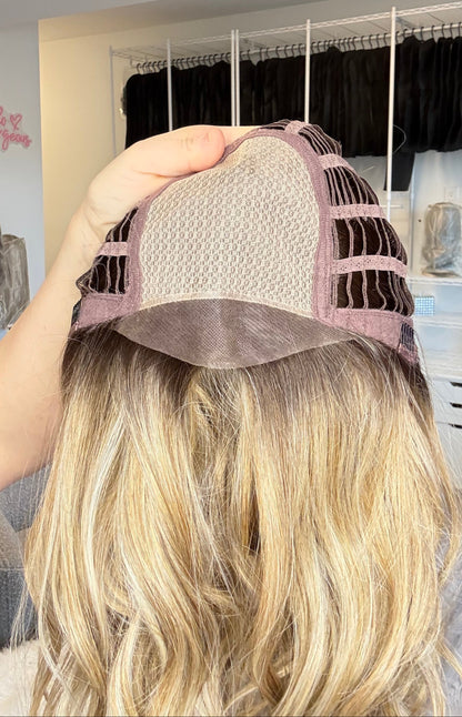 Person holding a blonde wig with a lace front in a store setting.
