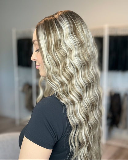 A person with long, wavy blonde hair in a room with wig racks.