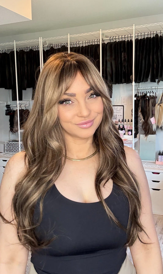 A dimensional light brunette wig with curtain bangs & long layered waves. Beginner-friendly non-lace Everyday Ready wig, customized in Alberta. Free shipping $150+.
