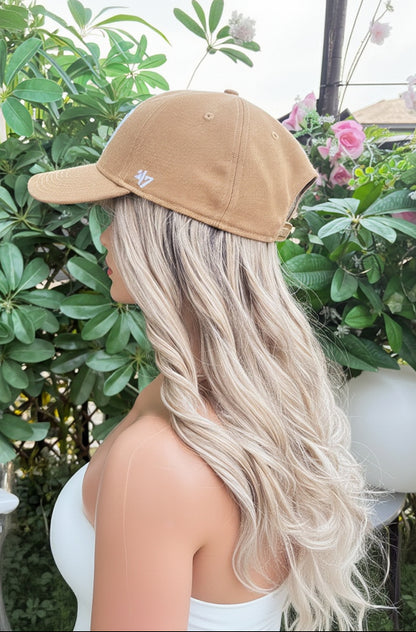 Mannequin head with blonde wig and beige cap against a floral and greenery background