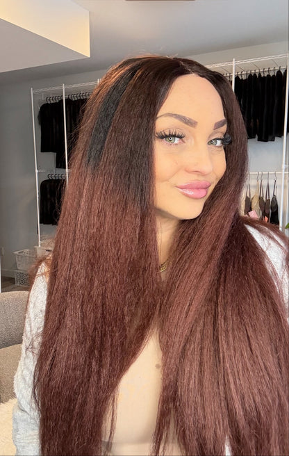 Woman with long brown wig in a room with clothing racks in the background