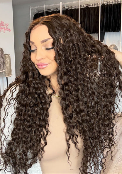 Woman with long, wavy hair extensions in a hair salon setting.