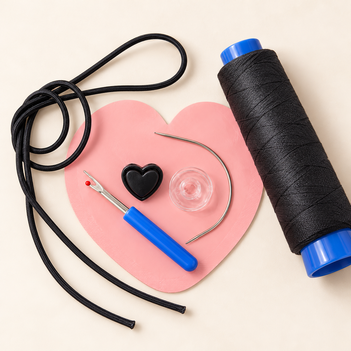 Black leather cord and a large spool of black thread with blue plastic ends, arranged on a pink heart-shaped mat with a blue-handled seam ripper, a small black heart-shaped tool, and a clear button on a light beige background.