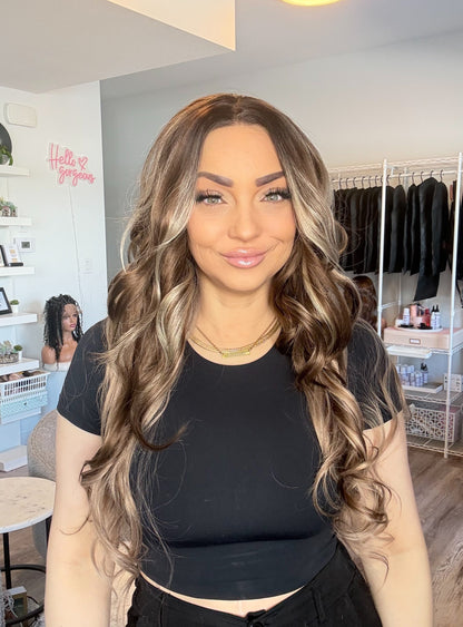 Woman with long, wavy hair in a room with clothing racks and shelves.