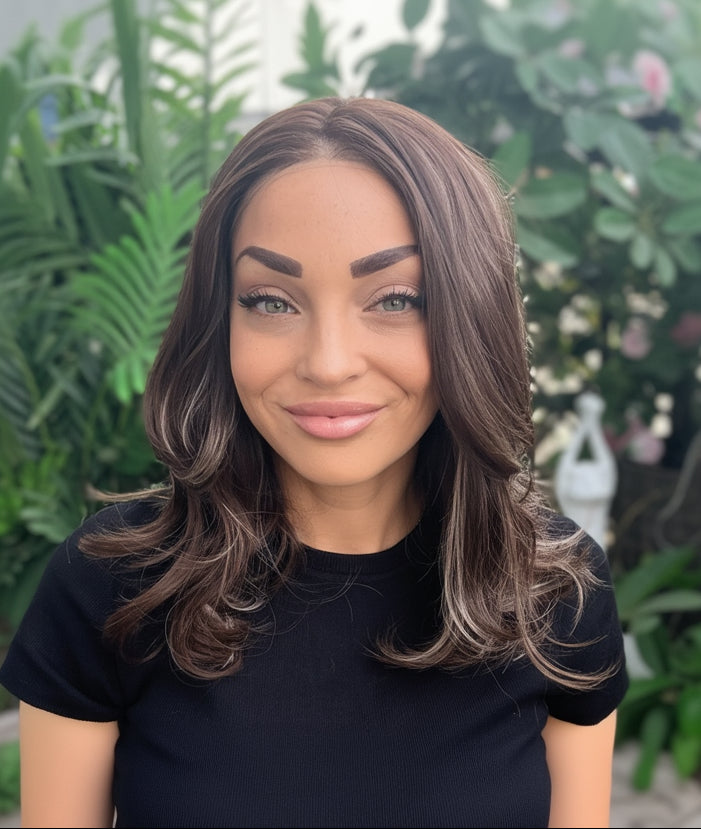 Woman with long, wavy hair sitting outdoors with greenery in the background