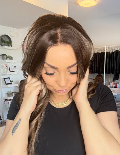 Woman adjusting a wig in a room with clothing racks and shelves.