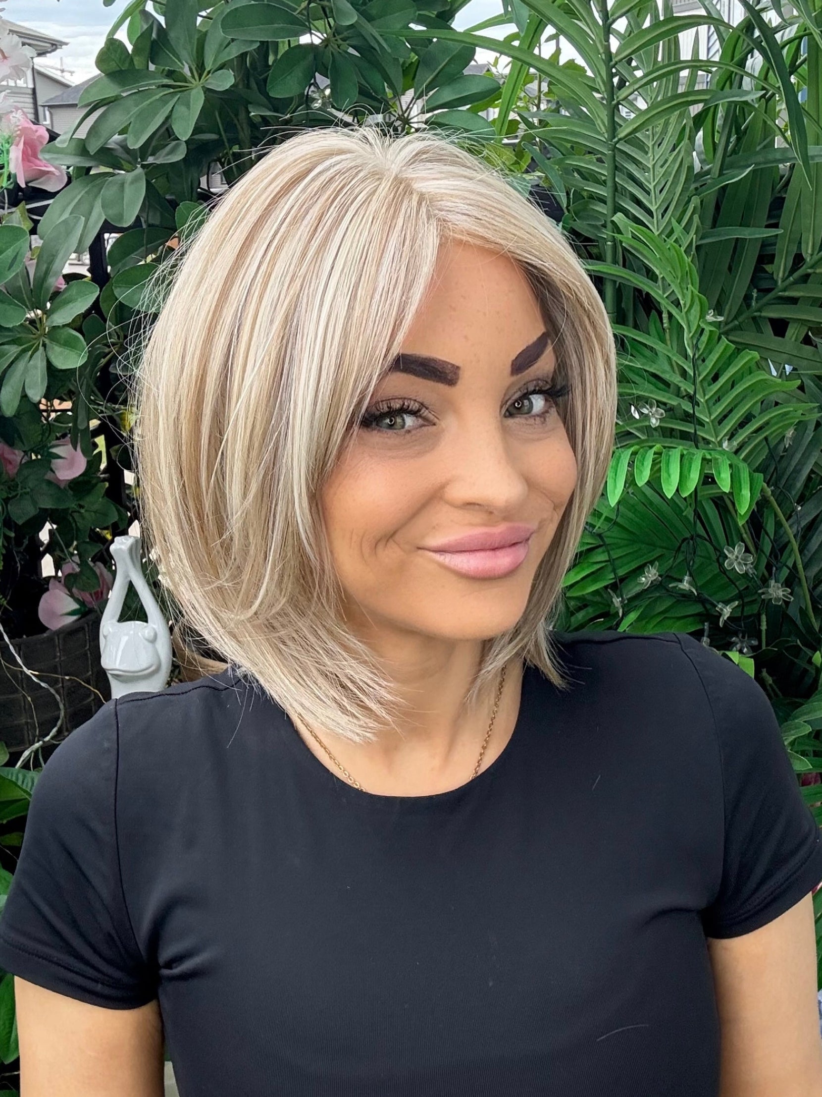 Woman with blonde hair and a black shirt standing in front of green foliage