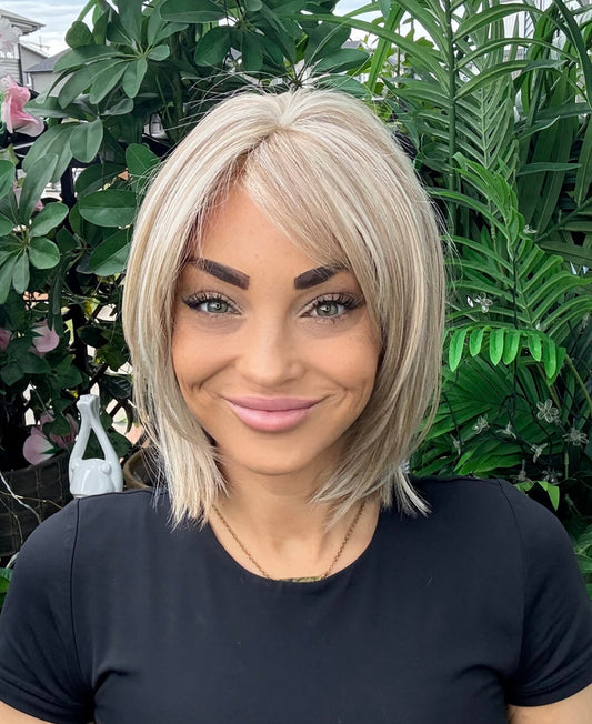 Woman with a short blonde hairstyle standing in front of green plants