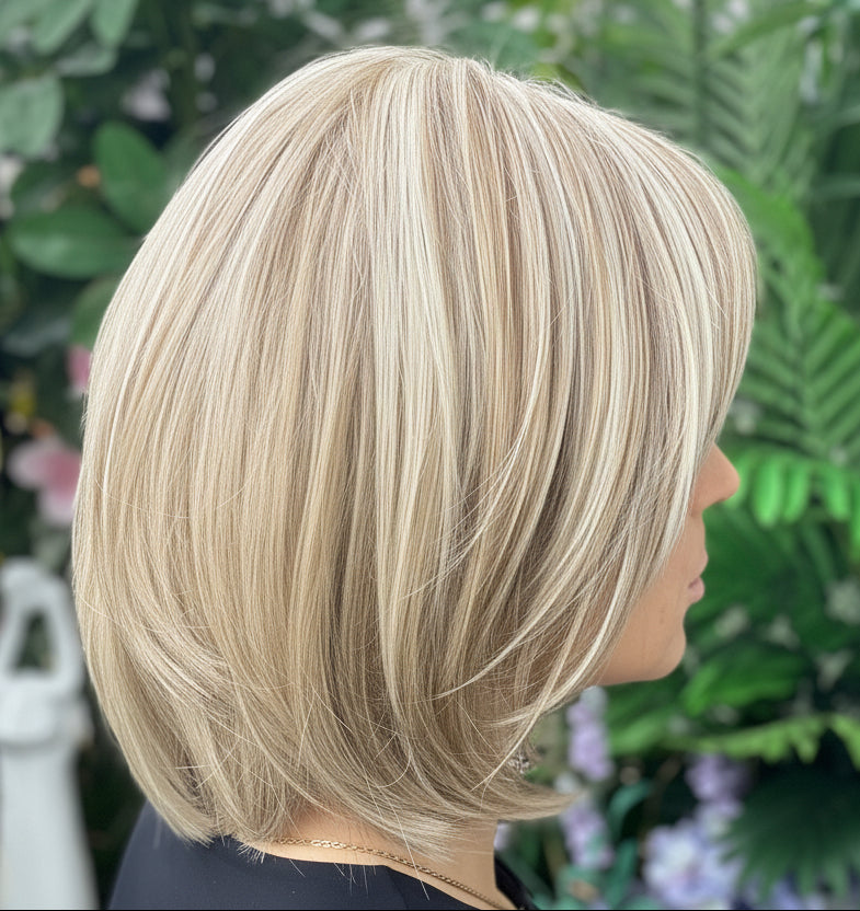 Person with a blonde bob haircut standing in front of green foliage and flowers