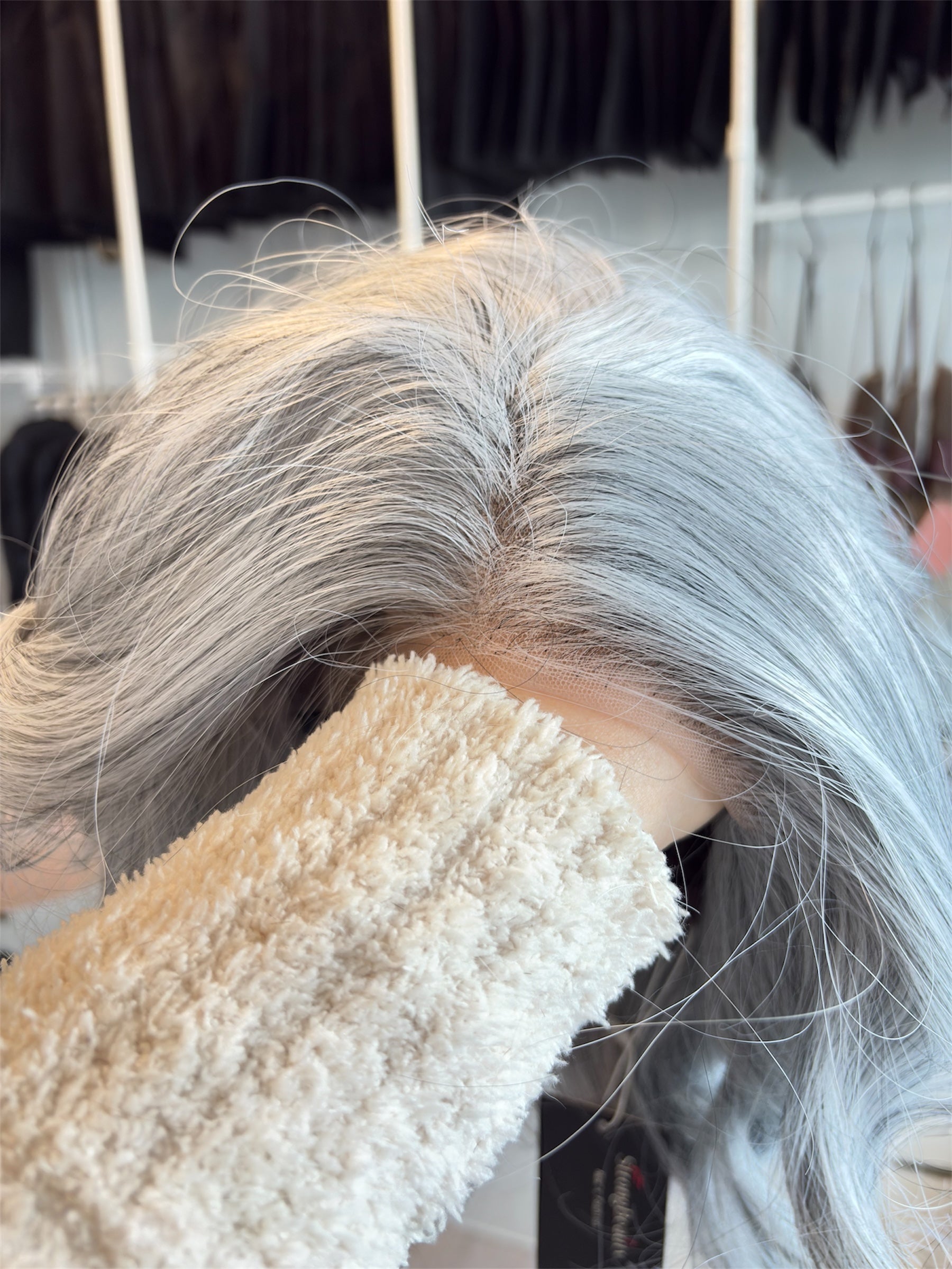 Close-up of a wig with gray hair being held by a textured beige hand towel.