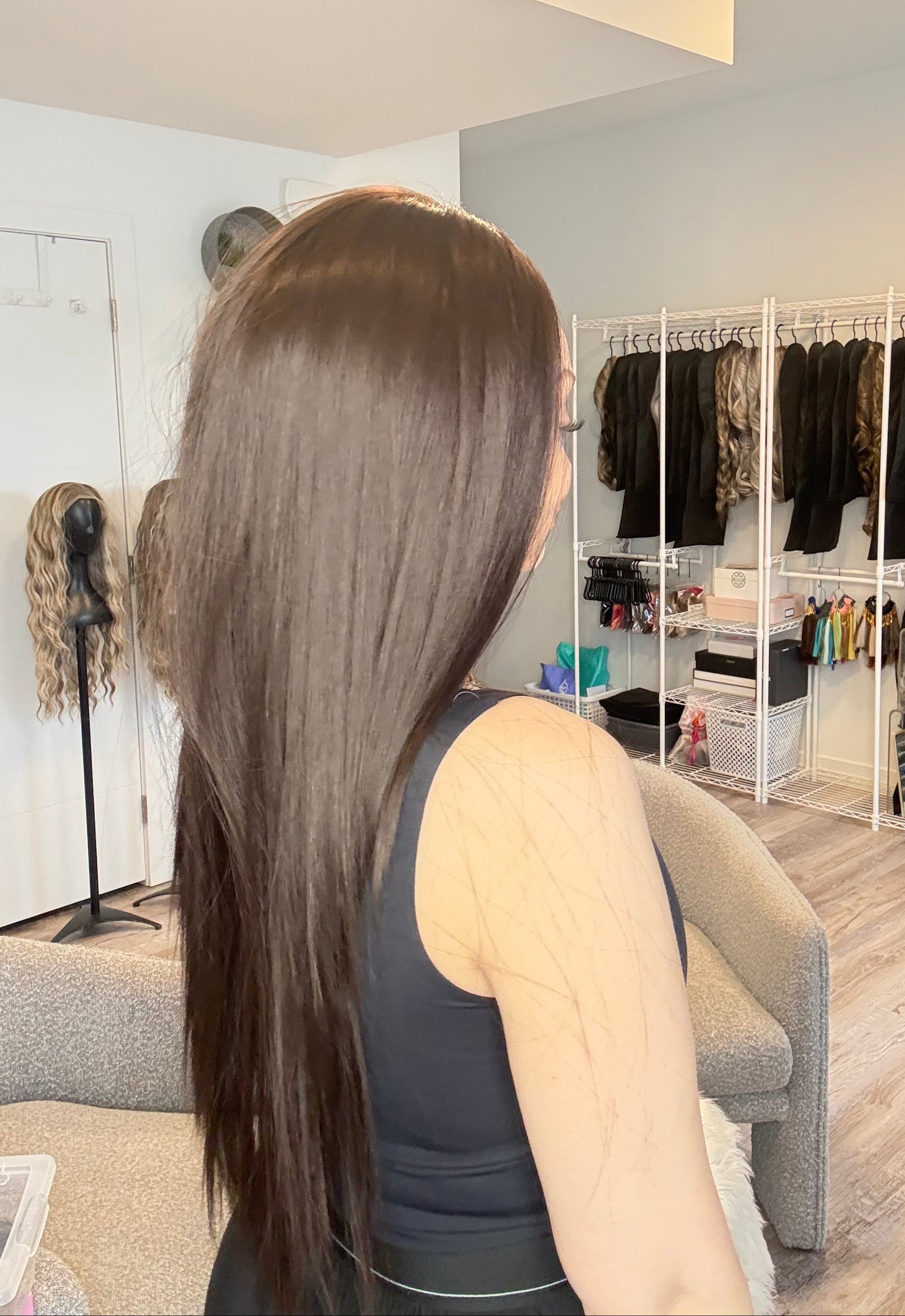 Person with long hair sitting in a salon chair, looking at themselves in the mirror.