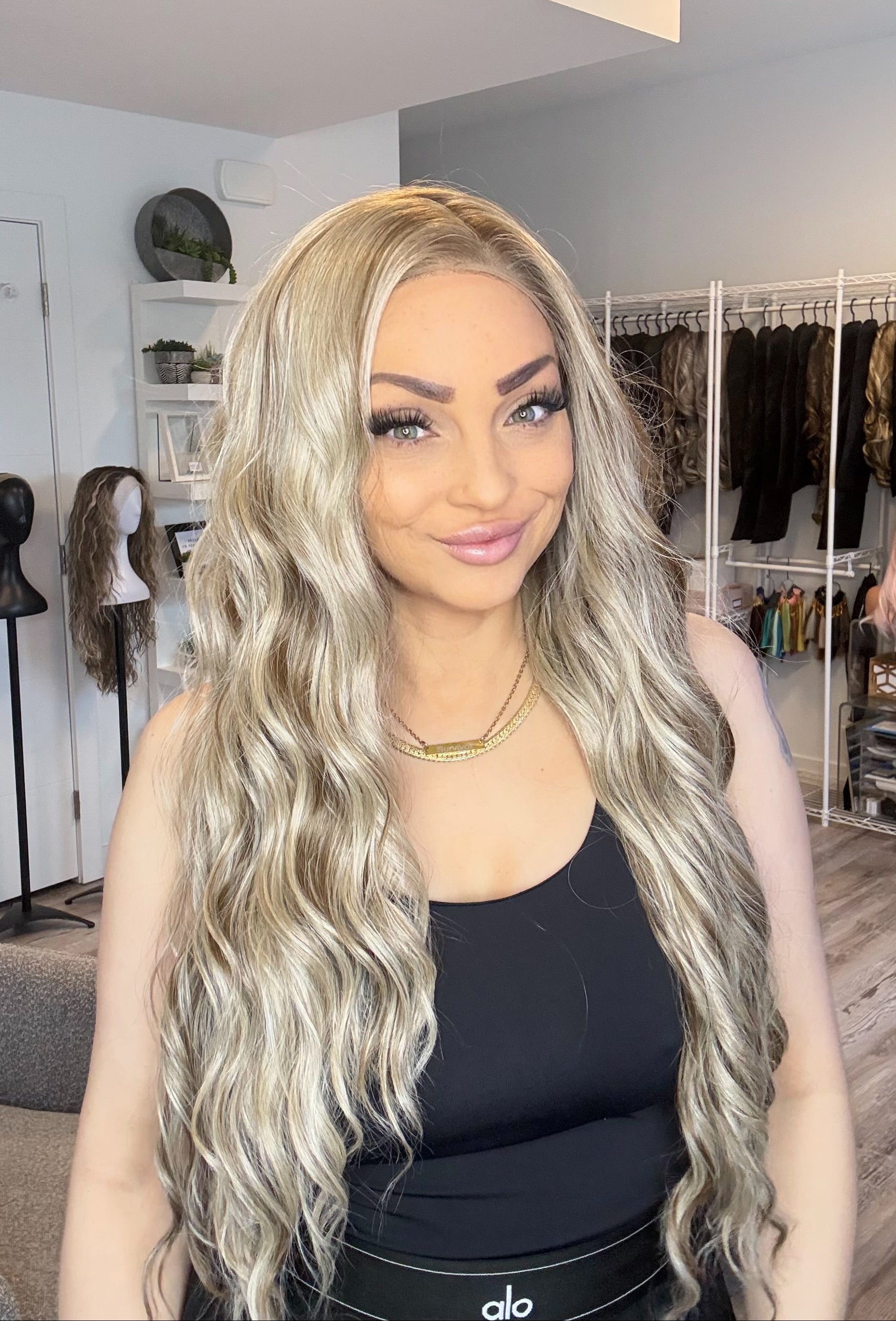 Person with long blonde wig in a room with mannequins and clothing racks.