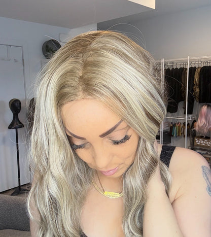 Person with long blonde hair in a room with clothing racks in the background