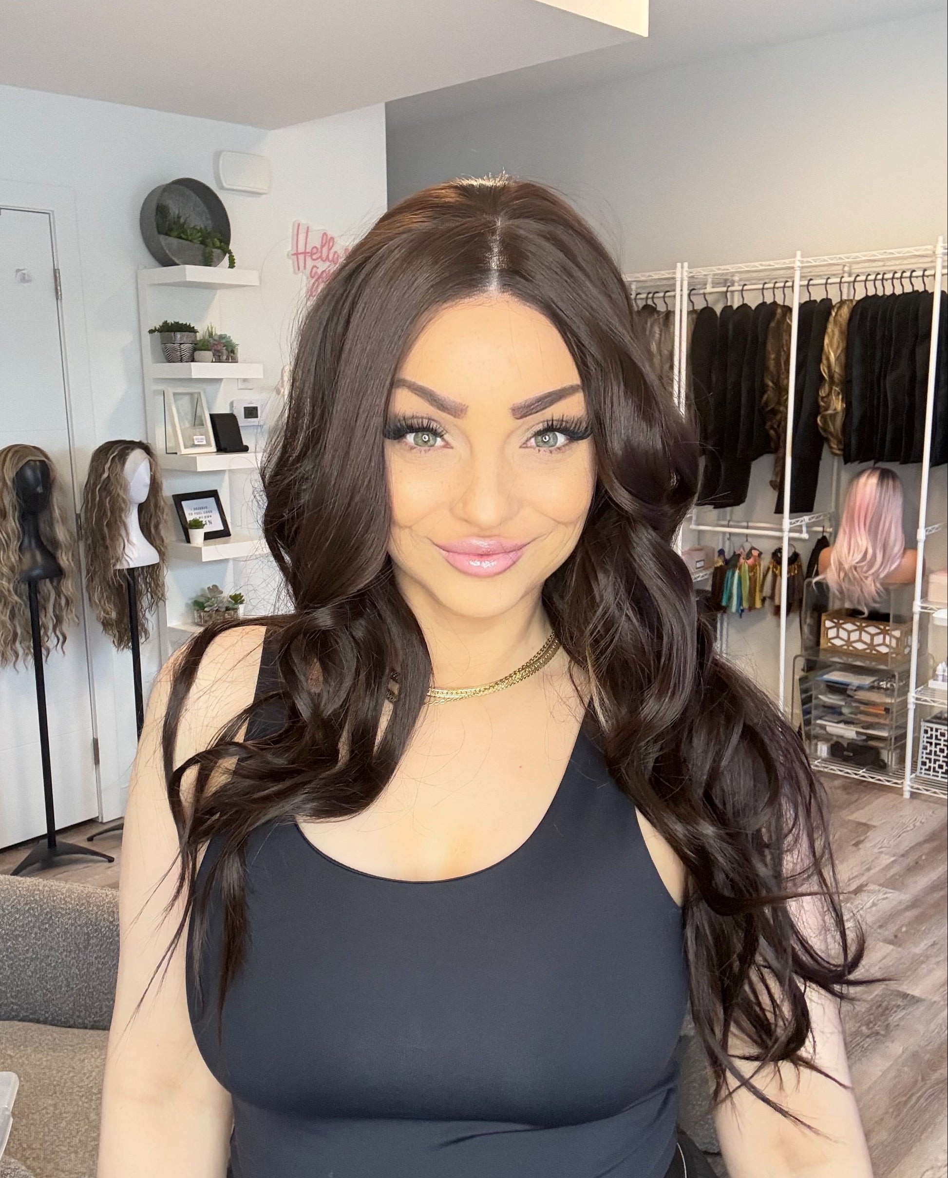 Woman with long dark hair in a salon setting with wigs on mannequins in the background.