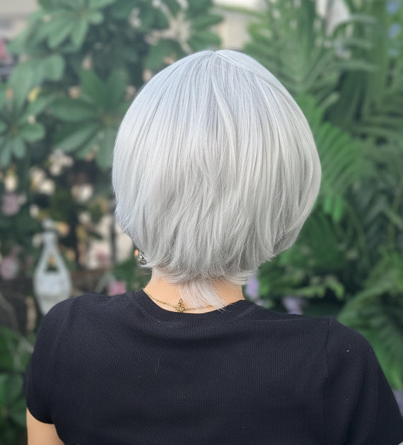 Person with white hair and a black shirt standing among greenery and flowers
