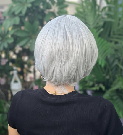 Person with white hair and a black shirt standing among greenery and flowers