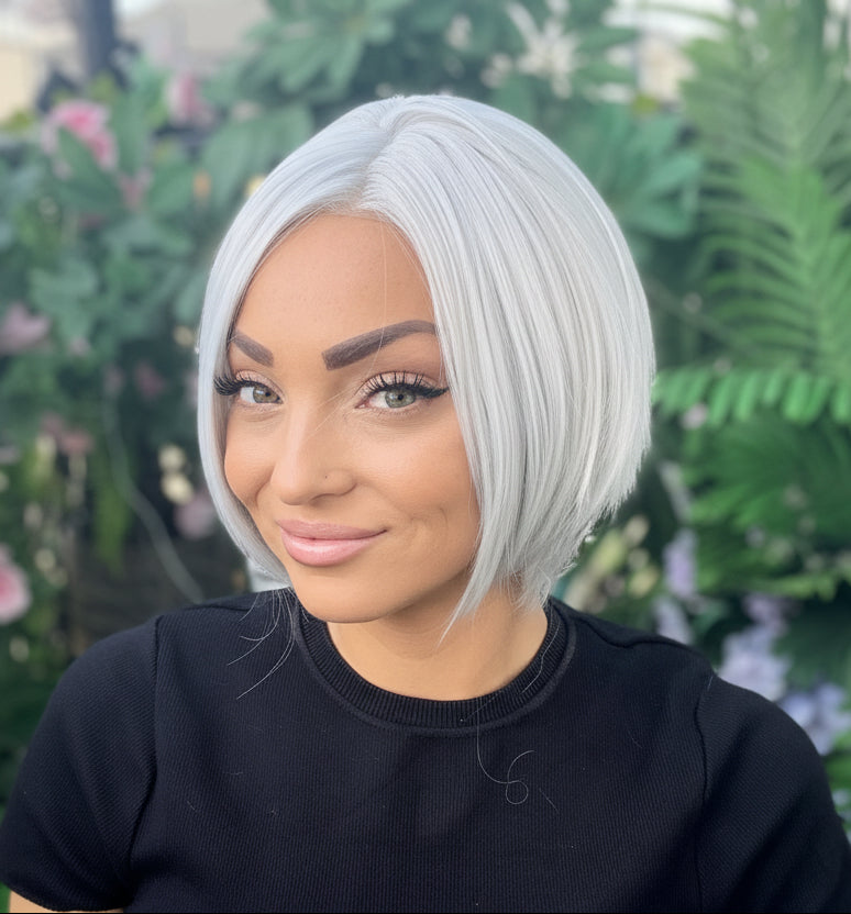 Woman with short silver hair wearing a black shirt in front of greenery and flowers