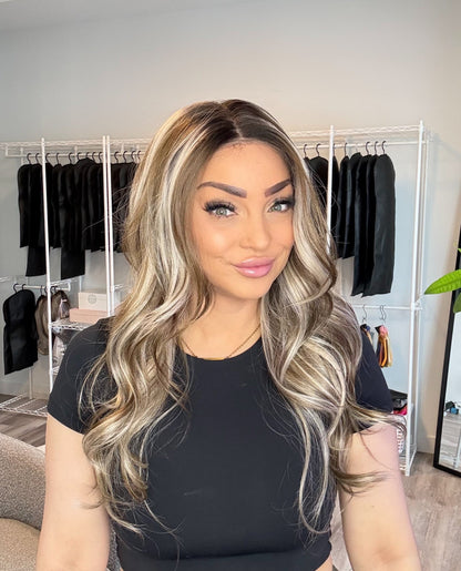 Woman with long, wavy hair in a room with clothing racks.