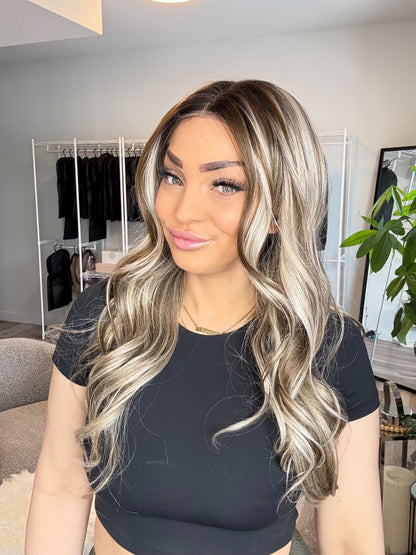Woman with long, wavy hair in a room with clothing racks and plants.