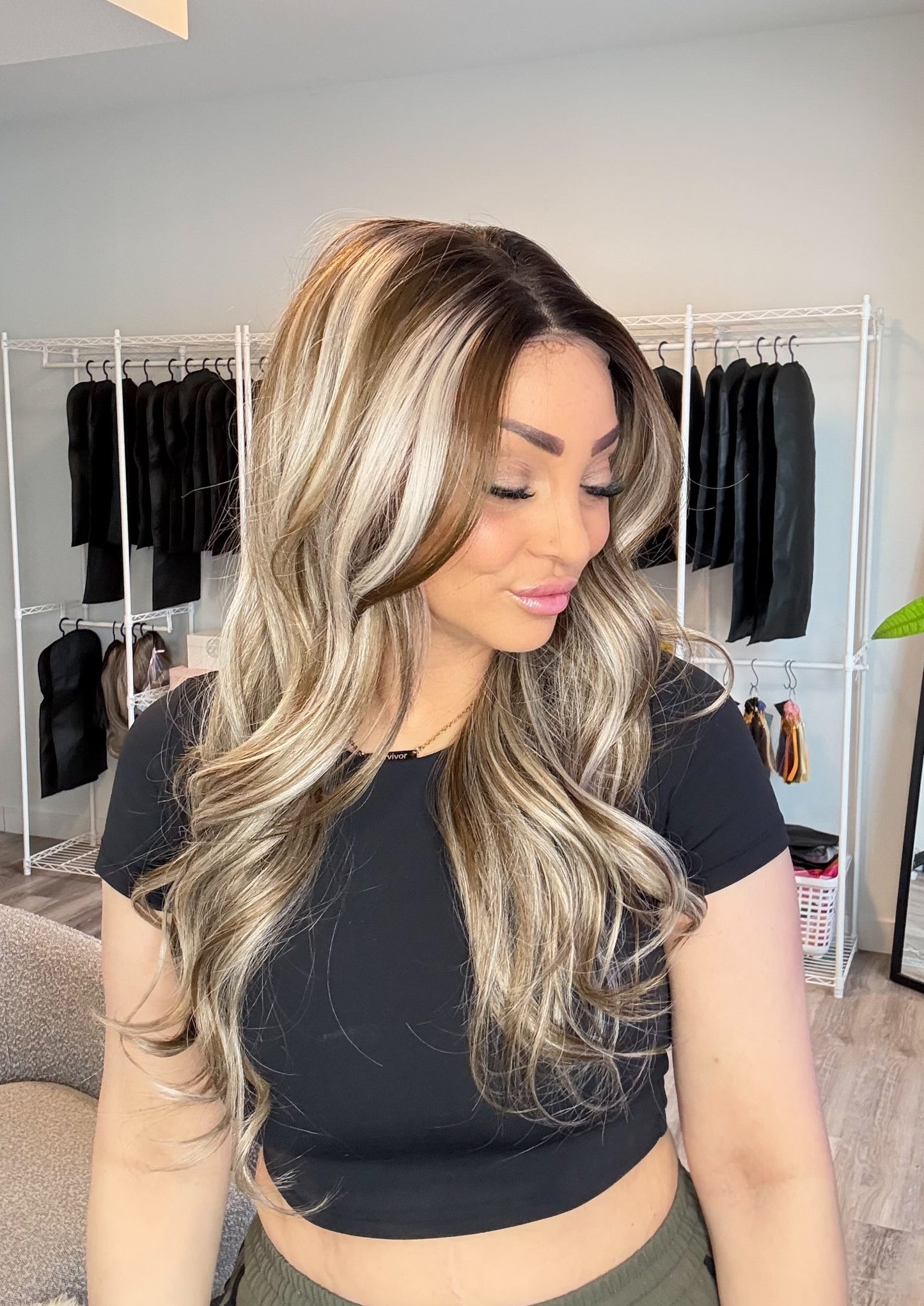 Woman with long, wavy hair in a room with clothing racks and a plant.