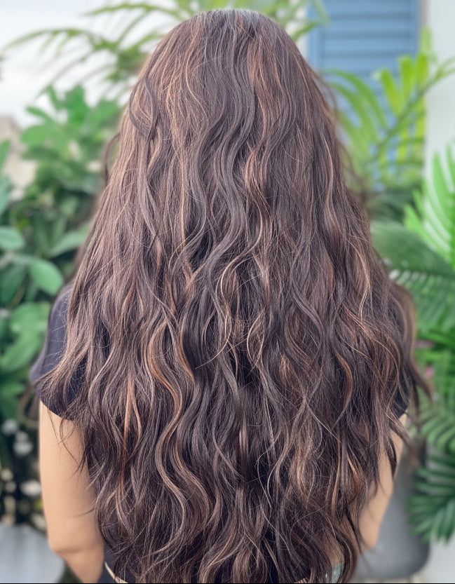 Person with long wavy hair standing outdoors with greenery around
