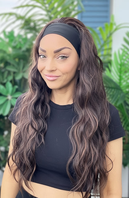 Woman with long wavy hair wearing a black headband and black top in front of green plants.