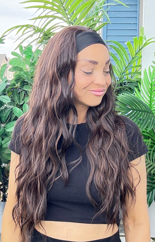 Woman with long wavy hair wearing a black top in front of green plants