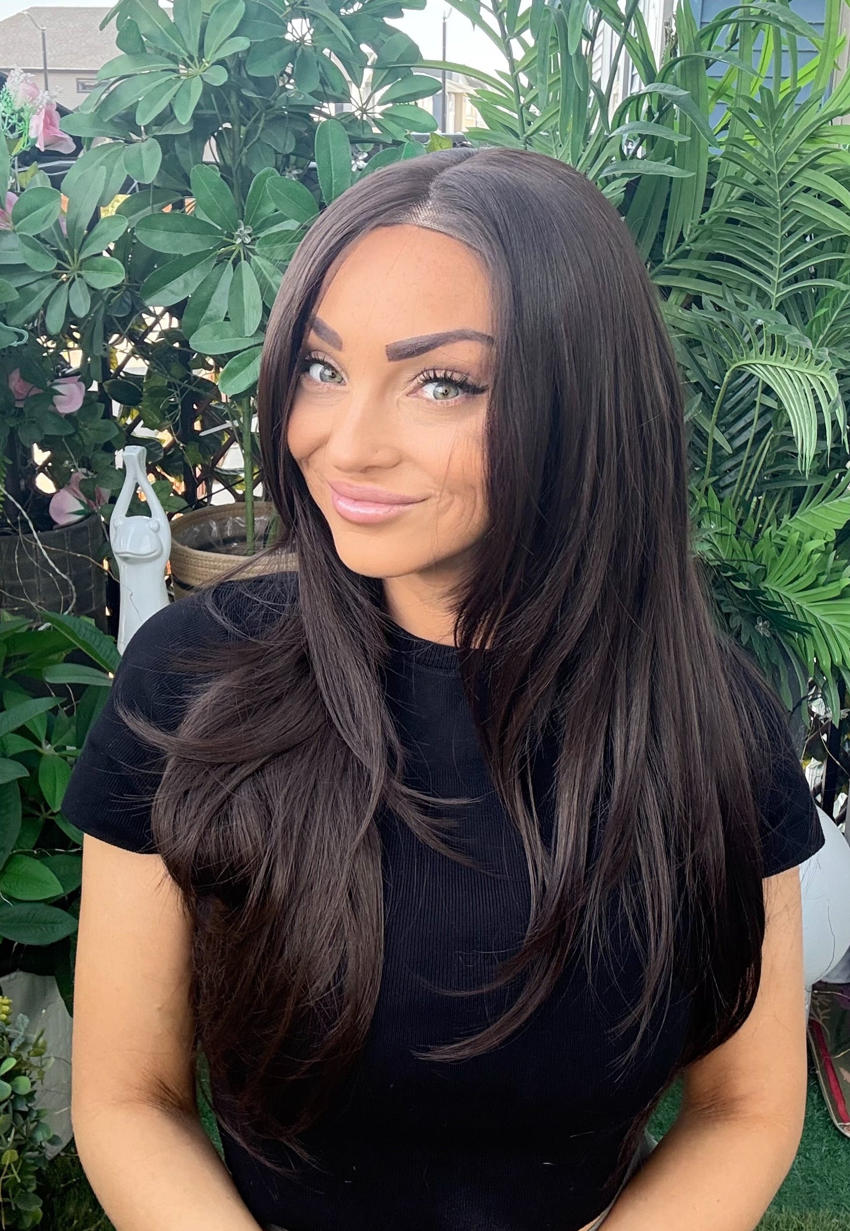 Woman with long dark hair standing outdoors among greenery