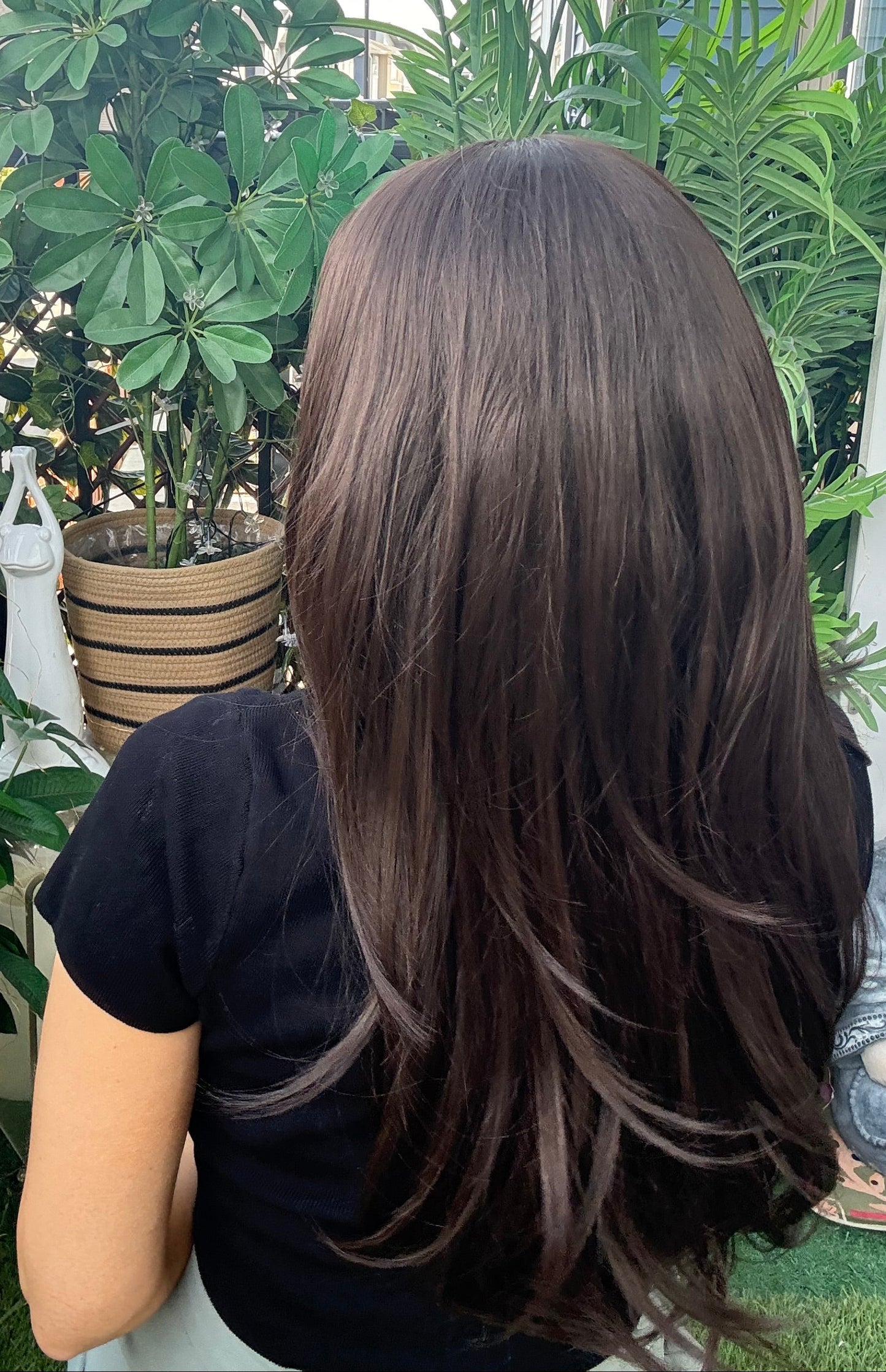 Person with long hair sitting outdoors with greenery in the background